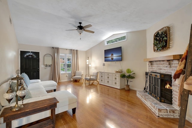 living room featuring wood-type flooring, vaulted ceiling, ceiling fan, and a brick fireplace