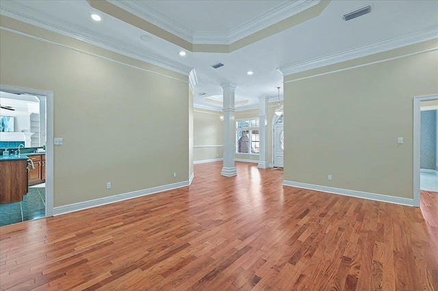 unfurnished living room with light wood-style floors, ornate columns, a tray ceiling, visible vents, and ornamental molding