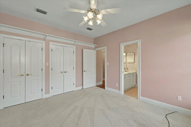 unfurnished bedroom featuring baseboards, light colored carpet, two closets, and visible vents
