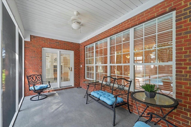 sunroom featuring carpet floors, wood ceiling, ceiling fan, and brick wall