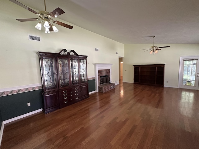 unfurnished living room featuring visible vents, dark wood-type flooring, a brick fireplace, and a ceiling fan