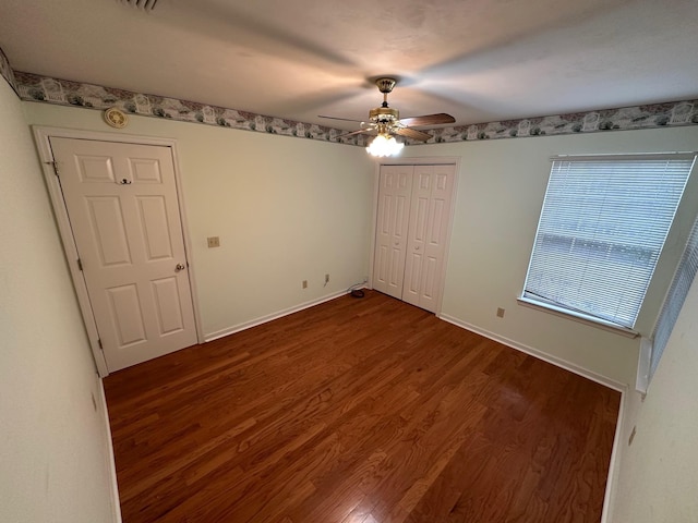 unfurnished bedroom with dark wood finished floors, baseboards, a closet, and ceiling fan