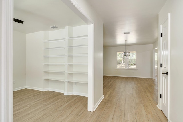 corridor with light hardwood / wood-style flooring and a notable chandelier