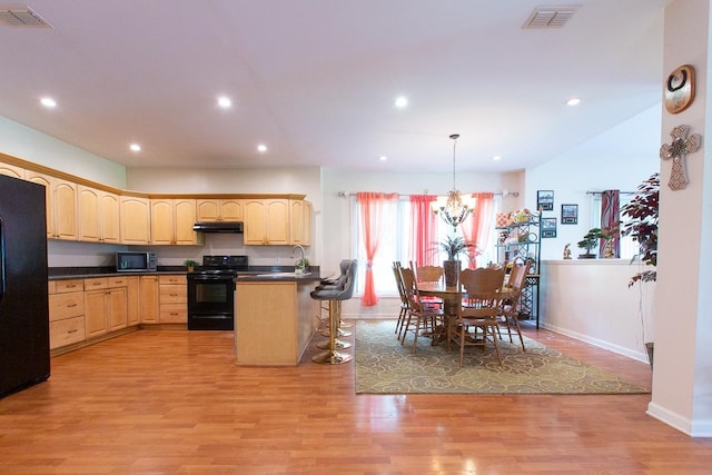 kitchen with black appliances, a chandelier, light brown cabinets, light wood-type flooring, and decorative light fixtures