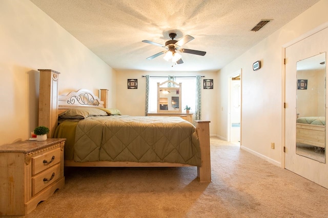 bedroom with a textured ceiling, light colored carpet, and ceiling fan