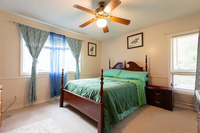 bedroom with ceiling fan, wooden walls, and light colored carpet