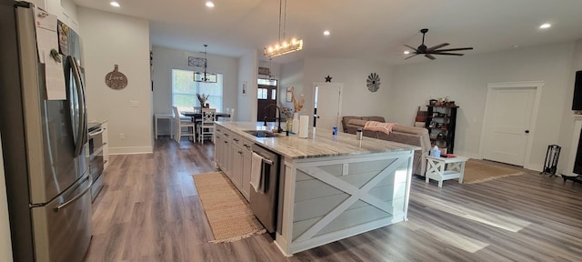 kitchen featuring appliances with stainless steel finishes, decorative light fixtures, sink, white cabinets, and a center island with sink