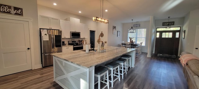 kitchen featuring appliances with stainless steel finishes, a breakfast bar, white cabinetry, hanging light fixtures, and a center island with sink