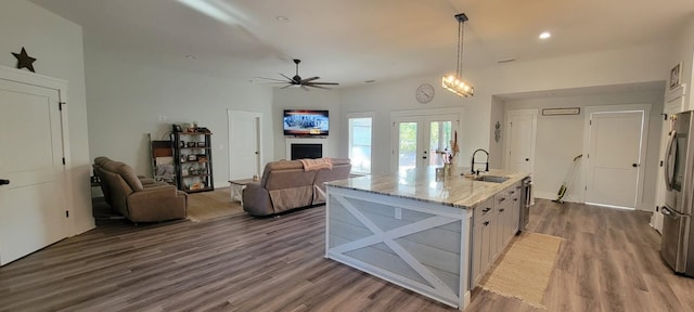 kitchen with dark hardwood / wood-style floors, an island with sink, sink, hanging light fixtures, and light stone countertops