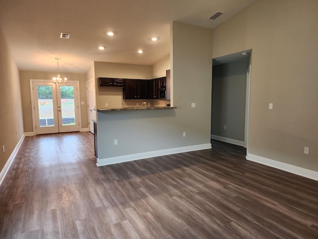 kitchen featuring dark brown cabinetry, dark hardwood / wood-style flooring, an inviting chandelier, stone countertops, and kitchen peninsula