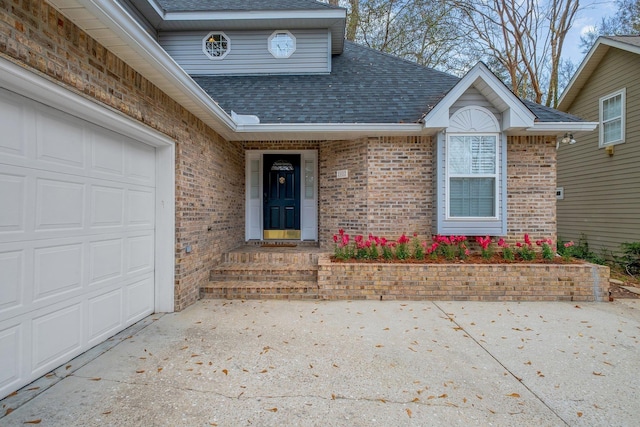 view of exterior entry featuring an attached garage, driveway, brick siding, and a shingled roof