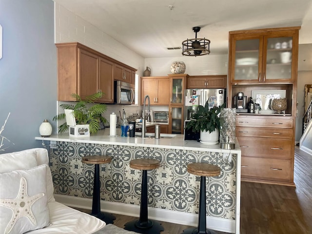 kitchen featuring glass insert cabinets, a breakfast bar, appliances with stainless steel finishes, and brown cabinets