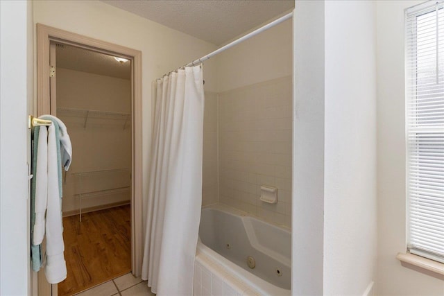 full bathroom featuring a combined bath / shower with jetted tub, a textured ceiling, and a spacious closet