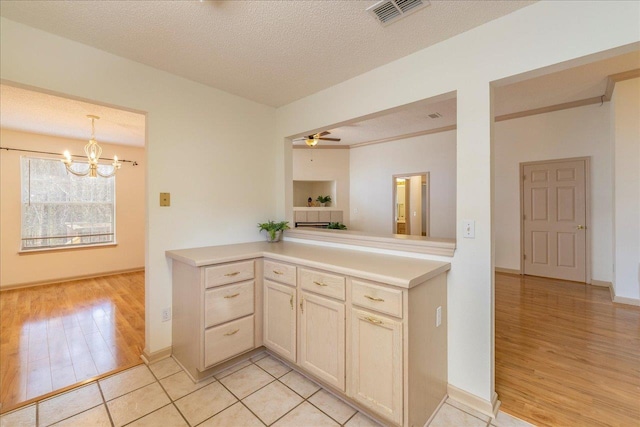 kitchen featuring a textured ceiling, visible vents, light countertops, hanging light fixtures, and light wood-type flooring