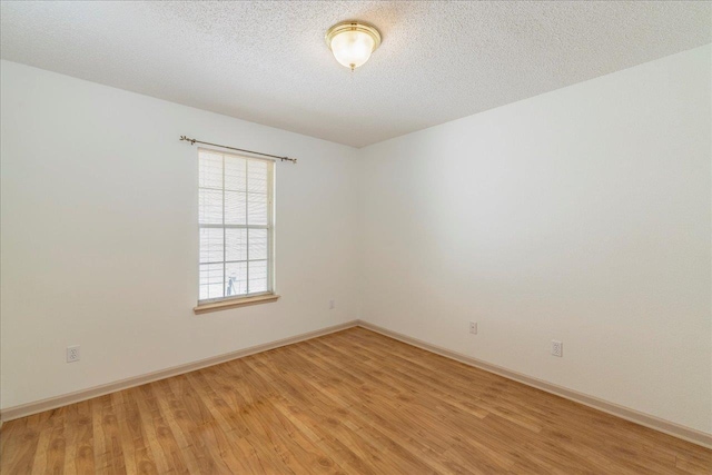 unfurnished room featuring light wood-type flooring, a textured ceiling, and baseboards