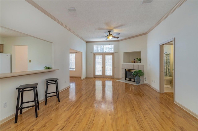 living area featuring baseboards, a textured ceiling, french doors, light wood-style floors, and a fireplace