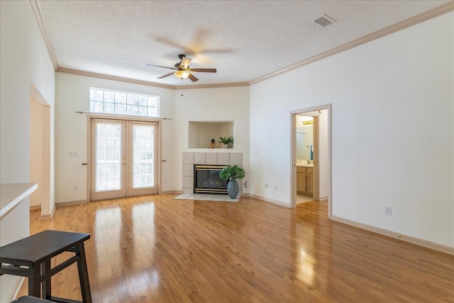 unfurnished living room featuring visible vents, a tile fireplace, light wood-style flooring, a textured ceiling, and crown molding