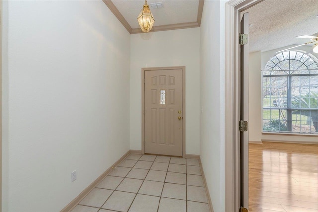 entryway with ornamental molding, light tile patterned flooring, a textured ceiling, and baseboards