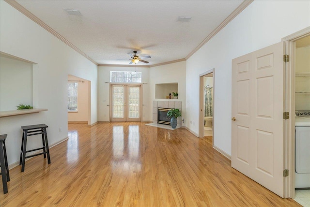 living room featuring ceiling fan, a fireplace, baseboards, ornamental molding, and light wood finished floors