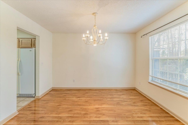 empty room featuring baseboards, a notable chandelier, light wood-style flooring, and a textured ceiling