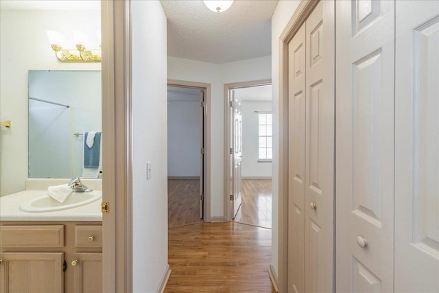 hallway with baseboards, a sink, light wood-style flooring, and a textured ceiling