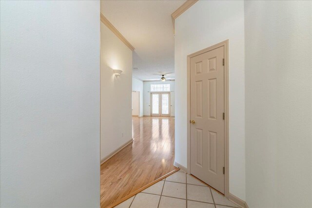 corridor featuring baseboards, crown molding, and light tile patterned flooring