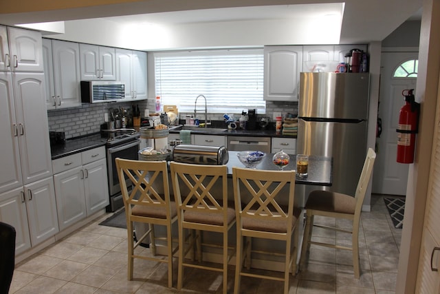 kitchen featuring stainless steel appliances, light tile patterned floors, sink, tasteful backsplash, and a breakfast bar area