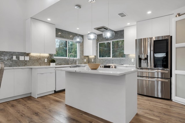 kitchen featuring decorative light fixtures, stainless steel fridge, a center island, and white cabinets