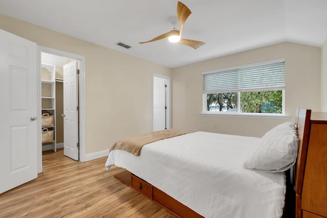 bedroom featuring lofted ceiling, a walk in closet, ceiling fan, light wood-type flooring, and a closet