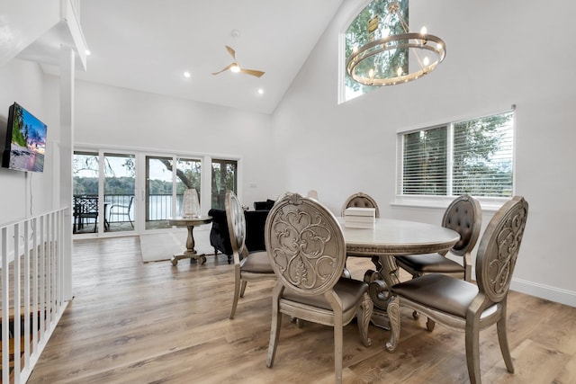 dining space with ceiling fan with notable chandelier, high vaulted ceiling, and light hardwood / wood-style floors