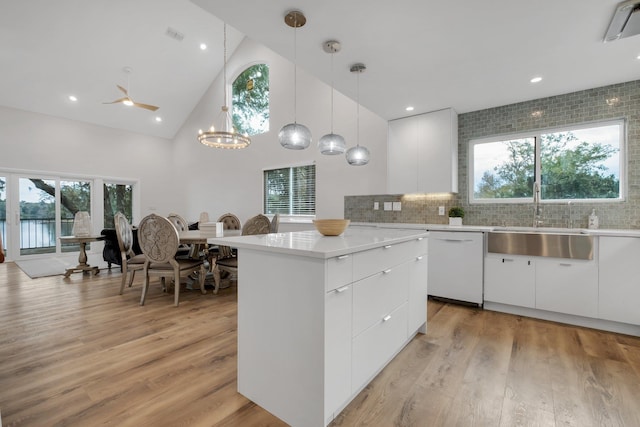 kitchen featuring sink, light wood-type flooring, white dishwasher, pendant lighting, and white cabinets