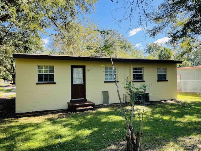 view of front of property with entry steps, concrete block siding, fence, and a front yard