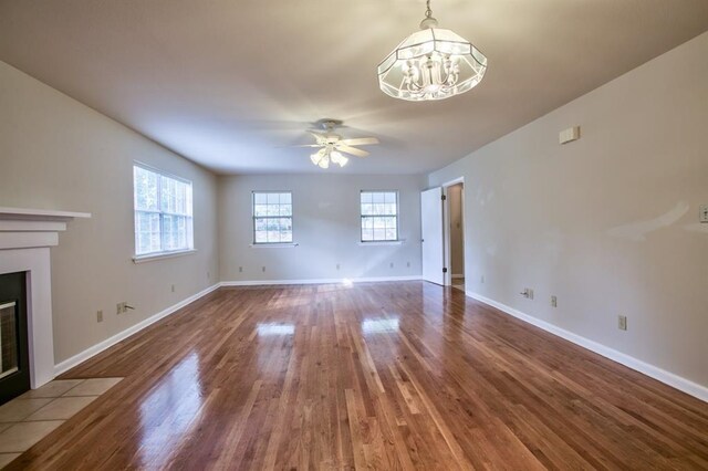 unfurnished living room with wood-type flooring, a healthy amount of sunlight, and ceiling fan with notable chandelier