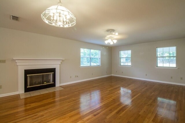 unfurnished living room featuring ceiling fan with notable chandelier, a wealth of natural light, and hardwood / wood-style flooring