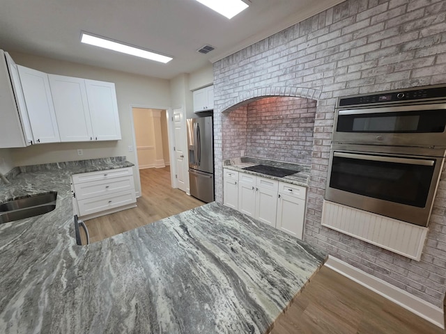 9369 Buck Haven Trl, Tallahassee, FL 32312 - kitchen with appliances with stainless steel finishes, light stone counters, light wood-style flooring, white cabinets, and brick wall