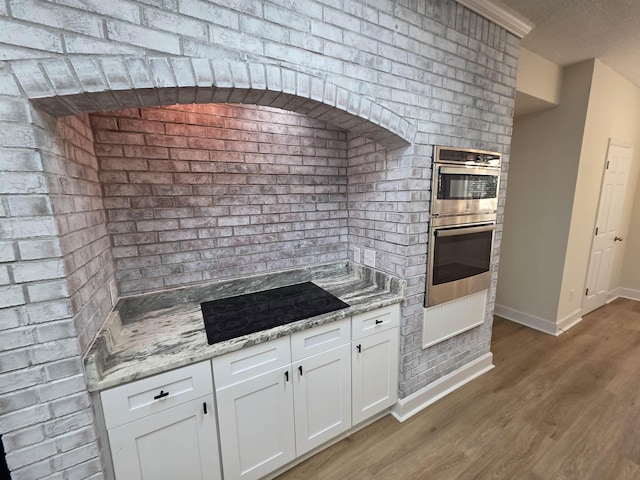 9369 Buck Haven Trl, Tallahassee, FL 32312 - kitchen with black electric stovetop, light wood-style flooring, white cabinets, stainless steel double oven, and light stone countertops