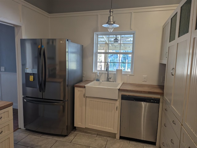 kitchen featuring appliances with stainless steel finishes, sink, light tile patterned floors, decorative light fixtures, and butcher block countertops