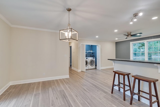 interior space featuring independent washer and dryer, light wood-style flooring, ornamental molding, a breakfast bar area, and baseboards