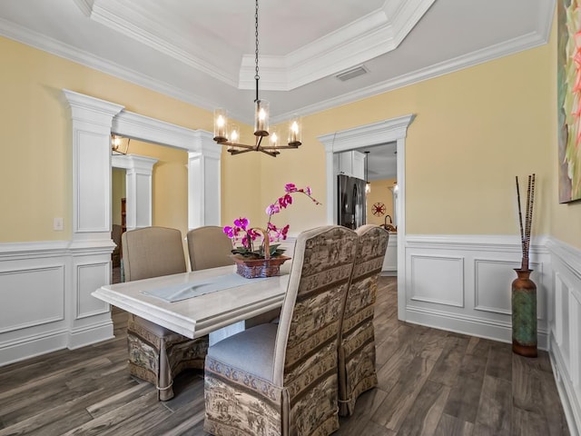 dining space featuring an inviting chandelier, a tray ceiling, dark hardwood / wood-style flooring, crown molding, and ornate columns