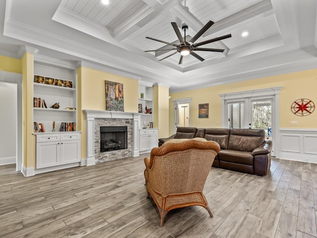 living room featuring light hardwood / wood-style flooring, built in shelves, a stone fireplace, crown molding, and a tray ceiling