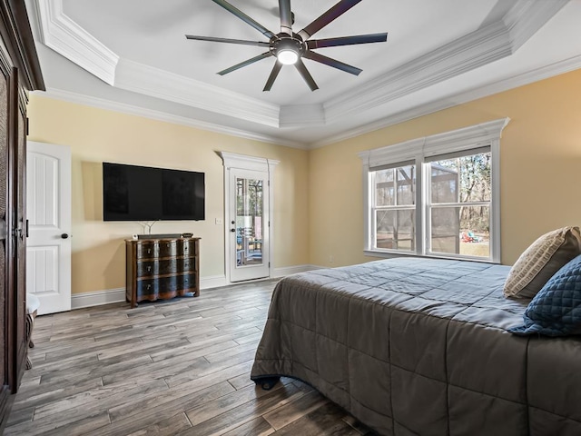 bedroom featuring hardwood / wood-style flooring, a tray ceiling, access to exterior, and ornamental molding