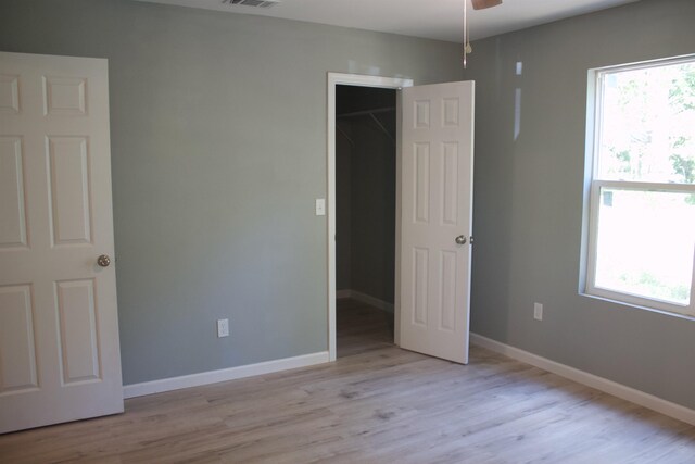 unfurnished bedroom featuring a closet, ceiling fan, a spacious closet, and light hardwood / wood-style floors