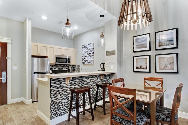 kitchen with decorative backsplash, appliances with stainless steel finishes, a kitchen breakfast bar, light hardwood / wood-style flooring, and hanging light fixtures