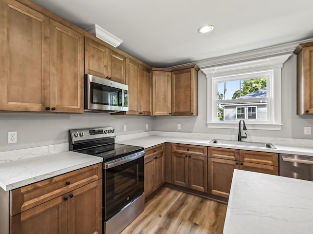 kitchen with light stone counters, sink, wood-type flooring, and appliances with stainless steel finishes