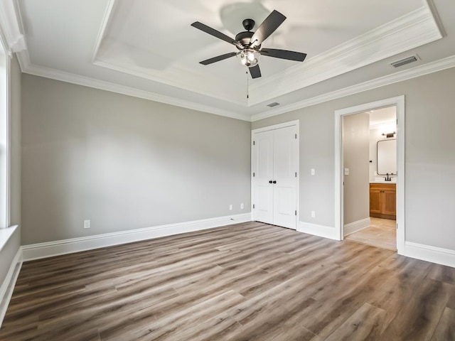 unfurnished bedroom featuring hardwood / wood-style floors, a tray ceiling, and ornamental molding