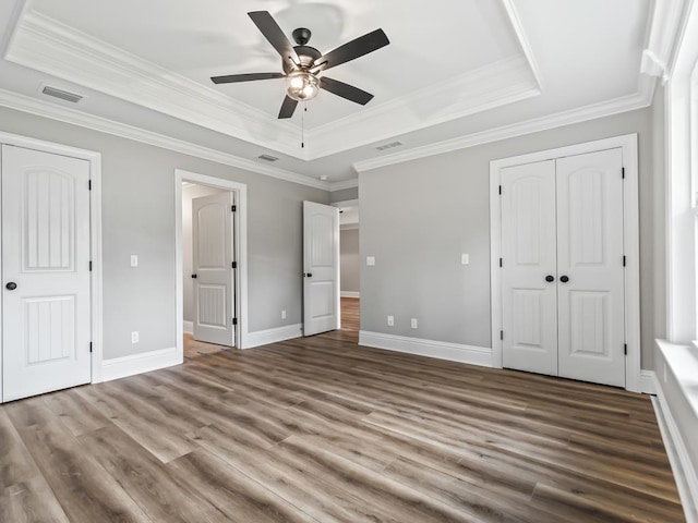 unfurnished bedroom featuring crown molding, a tray ceiling, ceiling fan, and hardwood / wood-style flooring