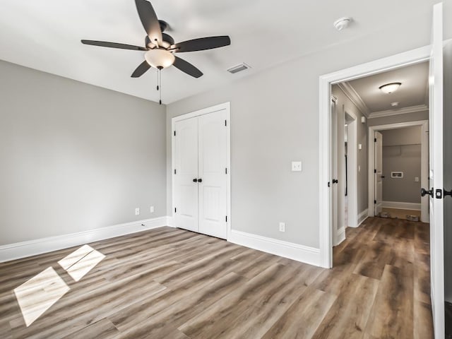 unfurnished bedroom featuring hardwood / wood-style flooring, ceiling fan, crown molding, and a closet