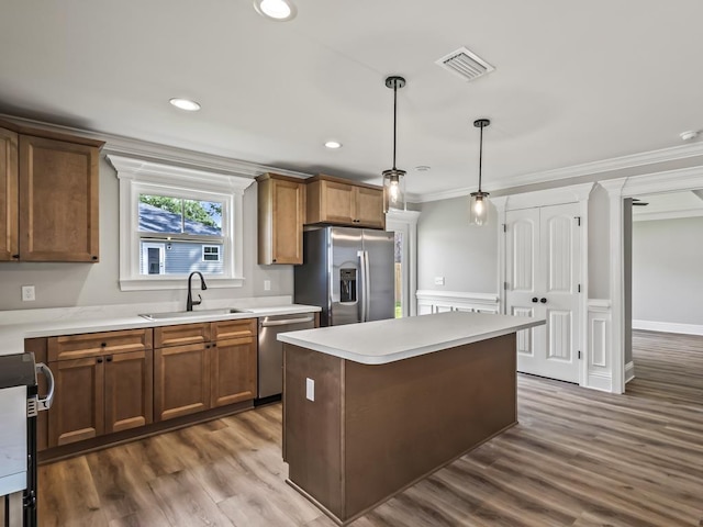 kitchen featuring sink, decorative light fixtures, ornamental molding, appliances with stainless steel finishes, and a kitchen island