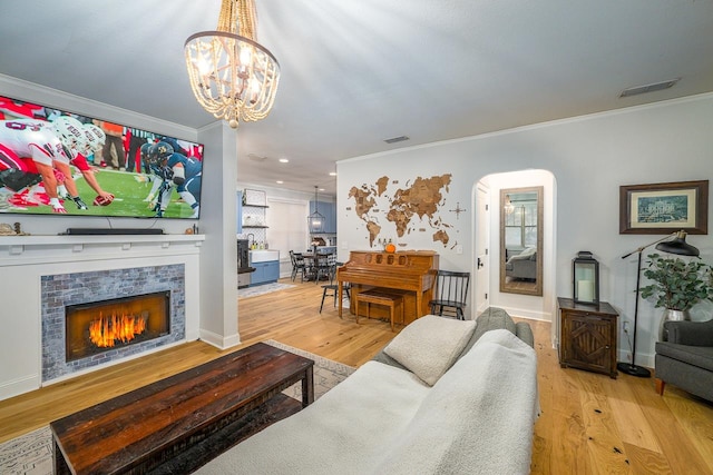 living room featuring a fireplace, an inviting chandelier, ornamental molding, and light hardwood / wood-style flooring