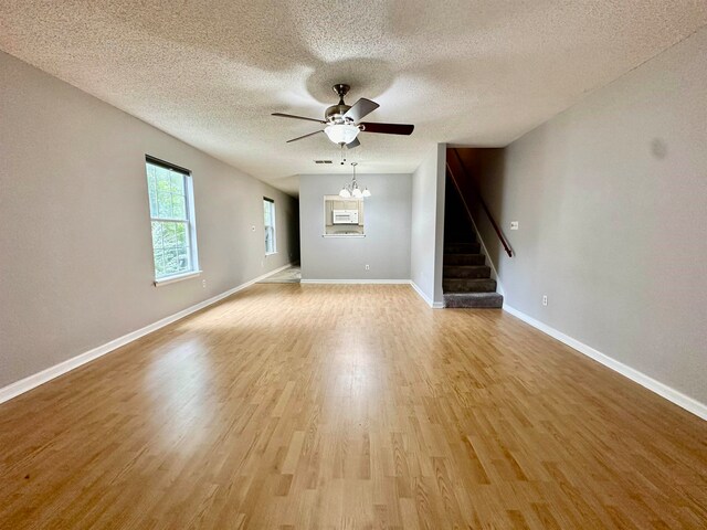 empty room featuring a textured ceiling, light hardwood / wood-style floors, and ceiling fan with notable chandelier